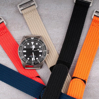Hook-and-loop single-pass watch straps in red, khaki, black, navy, and orange with Tudor diver on khaki strap