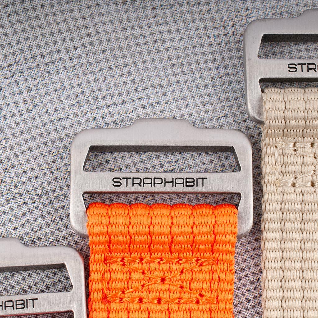 Close-up of StrapHabit branded buckle and hook-and-loop weave on orange and khaki single-pass straps