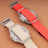 Two watches on hook-and-loop single-pass straps in khaki and red showing caseback and StrapHabit buckle